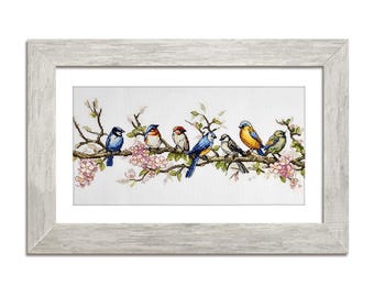 May include: A framed cross-stitch artwork featuring seven colorful birds perched on a flowering branch. The birds have blue, yellow, red, and green plumage. The artwork is set against a white background and framed in a light gray wooden frame.