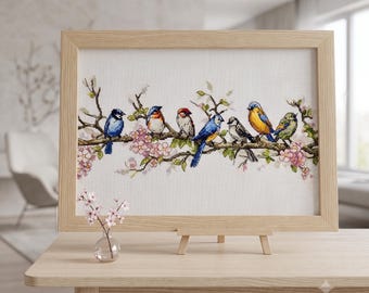 Op de afbeelding: Een ingelijst kruissteek borduurwerk met zeven kleurrijke vogels op een bloeiende tak met roze bloesems. Het kunstwerk staat in een lichtgekleurde houten lijst op een houten ezel, met een klein glazen vaasje met roze bloemen ernaast.
