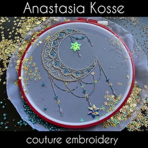 Puede incluir: Un bastidor de bordado con un diseño de media luna adornado con cuentas plateadas y turquesas y colgantes de estrellas. El texto "Anastasia Kosse" y "couture embroidery" es visible. Fondo gris.