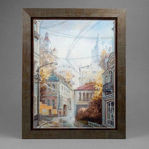 Könnte beinhalten: Ein gerahmtes Kreuzstichbild, das eine europäische Straßenszene mit mehrstöckigen Gebäuden, herbstlichem Laub und Stromleitungen zeigt. Das Kunstwerk befindet sich in einem strukturierten, dunkelbraunen Holzrahmen mit tiefem Innenrand.