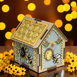 May include: A wooden house-shaped box with a bee and honeycomb design. The box is decorated with yellow and blue beads and has a clear plastic window.