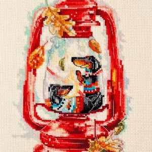 May include: A red lantern with two dachshund dogs inside. The lantern has a glass front and is decorated with fall leaves. The dogs are wearing sweaters and are looking out of the lantern.