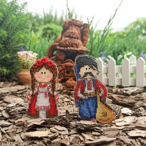 May include: Two embroidered figures in traditional Ukrainian clothing. A woman in a red and white dress with a floral crown and a man in a blue and red shirt holding a musical instrument.