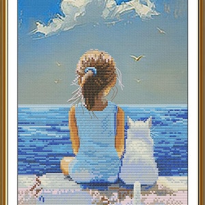 May include: Cross-stitch artwork depicting a girl in a blue dress and a white cat, seated and facing the ocean. The sky is blue with white clouds and birds. The artwork is framed in a gold-colored frame.