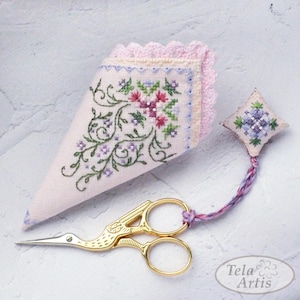 May include: A light pink needlework kit featuring a floral design. The kit includes gold scissors, a needlework holder, and a pincushion. The scissors are shaped like a bird. The needlework holder and pincushion have embroidered floral patterns.