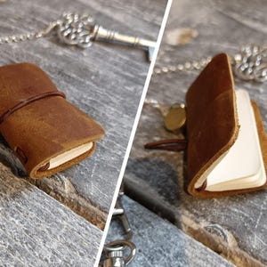 May include: A brown leather-bound journal with a silver chain and key attached. The journal is open to reveal blank pages.