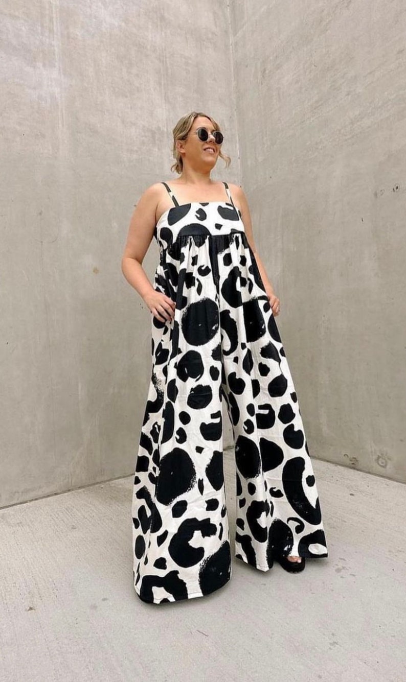 May include: A black and white jumpsuit with a large abstract print. The jumpsuit has a wide leg and a fitted bodice. The model is wearing the jumpsuit with black sandals.