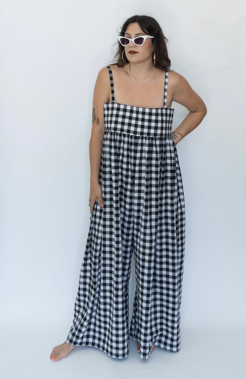 May include: A black and white gingham jumpsuit with thin straps. The jumpsuit has a square neckline and a loose, flowing fit.