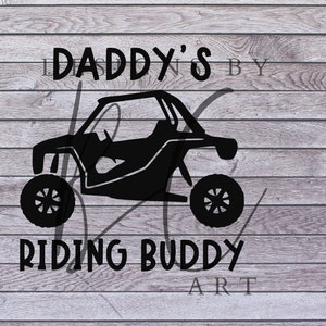 May include: Black and white silhouette of a side-by-side off-road vehicle with the text "Daddy's Riding Buddy" below it. The image is on a woodgrain background.