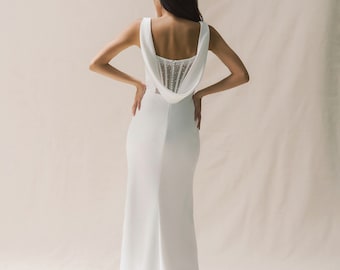 May include: A white sleeveless wedding dress with a fitted bodice and a flowing skirt. The back of the dress features a lace panel with a row of buttons.