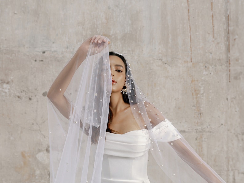 Bride in an off-shoulder satin wedding dress with a fitted bodice, thigh-high slit, and subtle train. Elegant and modern, with statement earrings and heels.