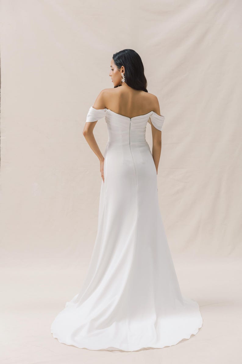 May include: A white off-the-shoulder wedding dress with a fitted bodice and a flowing skirt.