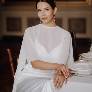 a modern bride wears sheer bridal cape made of light sheer chiffon