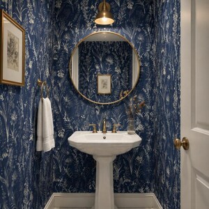 May include: A powder room featuring deep blue wallpaper with a white botanical print, a white pedestal sink with brass fixtures, a round brass-framed mirror, a brass wall sconce, a white towel on a brass ring, and a framed botanical print.