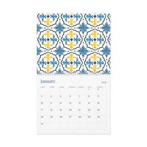 Our 2027 Azulejos wall calendar opened to January's calendar page with a beautiful blue and yellow floral tile pattern at the top. The calendar grid features days of the week starting with Sunday and the numbers for January.