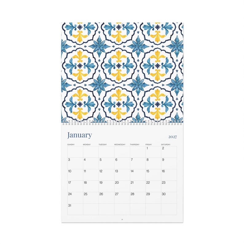 Our 2027 Azulejos wall calendar opened to January's calendar page with a beautiful blue and yellow floral tile pattern at the top. The calendar grid features days of the week starting with Sunday and the numbers for January.