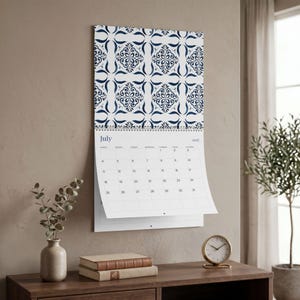Our 2027 Azulejos wall calendar opened to July 2027 calendar on a neutral wall, featuring a repeating blue and white tile pattern at the top. Below, the days of the week are displayed, with July 1st falling on a Thursday and the month ending on a Saturday.
