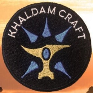 Peut inclure: Un écusson brodé noir et blanc avec le texte "KHALDAM CRAFT" en cercle autour d'une enclume dorée stylisée avec des accents bleus.