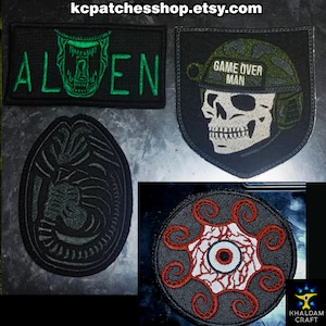 Könnte beinhalten: Eine Sammlung gestickter Aufnäher mit verschiedenen Designs. Ein Aufnäher zeigt das Wort "ALIEN" mit einem grünen Kreaturen-Design. Ein anderer zeigt einen Schädel mit Helm und dem Text "GAME OVER MAN". Weitere Aufnäher zeigen ein Alien-Ei und ein rundes Design mit einem Auge.