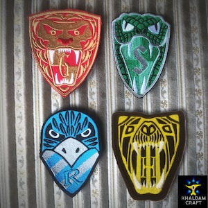 Może przedstawiać: Cztery haftowane łatki przedstawiające herby domów z serii Harry Potter. Herby to Gryffindor (lew), Slytherin (wąż), Ravenclaw (orzeł) i Hufflepuff (borsuk).