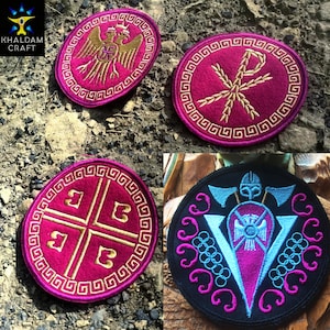 Może przedstawiać: Cztery haftowane naszywki z różnymi wzorami. Trzy są w kolorze magenta ze złotym haftem, przedstawiające dwugłowego orła, symbol Chi-Rho i krzyż. Czwarta jest czarna z niebieskim i magenta haftem, przedstawiająca motyw wikingów.