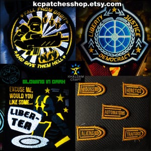 Op de afbeelding: Verzameling geborduurde patches met diverse ontwerpen. Eén patch toont een soldaat met de tekst "FALL FROM ORBIT" en "AND GIVE THEM HELL". Een andere toont een blauw embleem met "LIBERTY JUSTICE DEMOCRACY". Andere patches zeggen "BUGS", "HERETICS", "ALIENS", "AUTOMATONS" en "TRAITORS".
