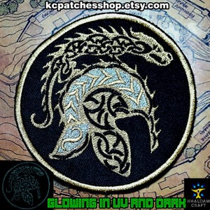 Może przedstawiać: Okrągła, czarna naszywka ze złotym i jasnoniebieskim wzorem smoka. Smok jest haftowany ze skomplikowanymi detalami. Naszywka ma złotą obwódkę i napis "GLOWING IN UV AND DARK". Nazwa sklepu Etsy "kcpatches shop" znajduje się u góry.