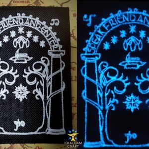 Op de afbeelding: Een zwarte stoffen patch met witte borduurwerk die een boog voorstelt met de woorden "Speak Friend and Enter" erboven. De boog is omgeven door wijnstokken en sterren. De patch gloeit blauw in het donker.