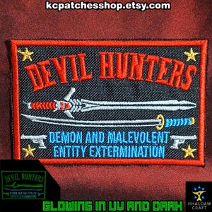 May include: Embroidered patch with the text "DEVIL HUNTERS" in red, featuring swords and guns. The patch also includes the text "DEMON AND MALEVOLENT ENTITY EXTERMINATION" and glows in UV and dark.