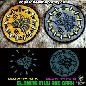 Peut inclure: Deux patchs brodés ronds représentant une tête de loup avec un motif jaune et gris. Les patchs brillent dans le noir et sous la lumière UV. Le texte "GLOWING IN UV AND DARK" est imprimé sous les patchs.