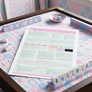 May include: A wooden mahjong table with brass corner accents, featuring a pastel pink and blue patterned surface. The table includes matching tile racks, a small bowl with two dice, and a printed instruction sheet titled American Mah Jongg.