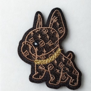 May include: Embroidered patch featuring a stylized French Bulldog. The dog is brown with a repeating pattern and a gold collar. The patch has a black border and a light blue eye.