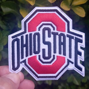 Peut inclure: Écusson brodé avec le logo de l'Université d'État de l'Ohio. Le patch a un "O" rouge au centre, avec les mots "OHIO STATE" en lettres blanches. Le patch est bordé de noir et de blanc.