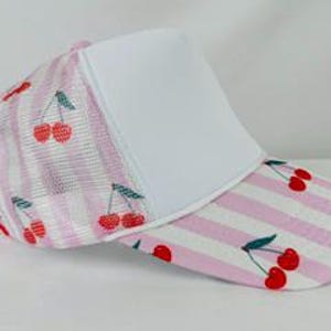 Puede incluir: Gorra de camionero a rayas rosas y blancas con un panel frontal blanco. La gorra presenta un patrón de cerezas en la visera y laterales de malla. Las cerezas son rojas con tallos verdes.