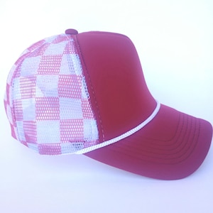 Könnte beinhalten: Burgunderfarbene Trucker-Cap mit weiß-rosa kariertem Mesh-Rückenteil und passendem burgunderfarbenem Vorderteil. Mit weißem Seildetail am Rand und kleinem burgunderfarbenem Knopf oben.