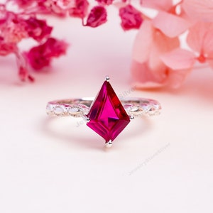 May include: A silver ring featuring a vibrant red, faceted, kite-shaped gemstone. The ring band has a delicate, beaded design.