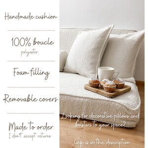 May include: A handmade, off-white boucle cushion with two matching decorative pillows. The pillows and cushion are made of 100% polyester with foam filling and removable covers. A wooden tray with muffins and a white mug sit on the cushion.