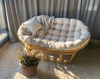 May include: A beige and brown wicker chair with a white cushion and a fluffy throw blanket. The chair is sitting on a beige carpet.