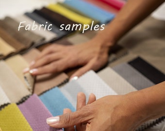Op de afbeelding: Een persoon bekijkt stofstalen in verschillende kleuren en texturen. De stalen liggen op een tafel en de persoon houdt een van de stalen in de hand. De tekst "Fabric samples" staat op de tafel.