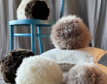 May include: Five fluffy round pillows in various shades of brown and white. The pillows are arranged on a light gray carpet in front of a blue wooden chair.