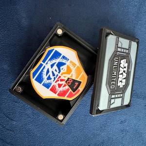 Pode incluir: Uma caixa de plástico preta com um logotipo Star Wars Unlimited na tampa. A caixa contém uma roda giratória colorida com um gráfico de personagem Star Wars e o número 81.