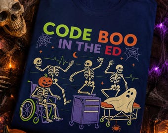 Pode incluir: Uma t-shirt azul-marinho com o texto "CODE BOO IN THE ED" em verde, laranja e vermelho. O gráfico inclui três esqueletos, um com cabeça de abóbora numa cadeira de rodas, um carrinho médico roxo e um fantasma numa maca de hospital.
