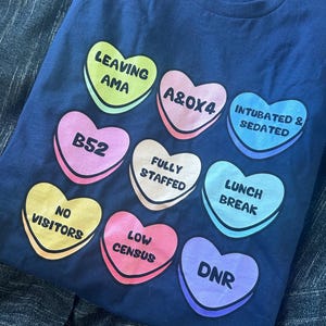Funny nurse Valentine shirt featuring candy hearts with medical terms like “A&Ox4,” “B52,” and “Fully Staffed.” Perfect nurse humor tee for Valentine’s Day or any shift. Made on comfy Gildan 5000 unisex shirts with high-quality print. Ideal gift for nurses, techs, or healthcare workers who love a laugh. Support a fellow nurse and grab this sweet and sassy hospital-themed shirt today!