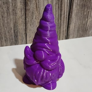 May include: A vibrant purple gnome figurine with a pointed hat, beard, and round body. The gnome is a decorative item, likely for a garden or shelf. The figurine is made of a solid material and has a textured surface.