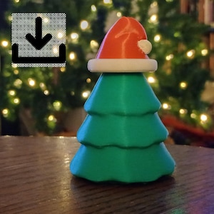 以下が含まれることがあります： 緑色のクリスマスツリーの置物。赤いサンタ帽、白いトリム、白いポンポンが付いています。ツリーは段になったデザインで、木製の表面に置かれています。背景はぼやけたクリスマスライトです。