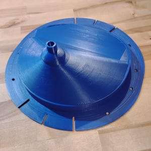 May include: A vibrant blue, 3D-printed object with a circular design. It features a central conical element and a series of evenly spaced slots around the perimeter. The object is made of plastic.