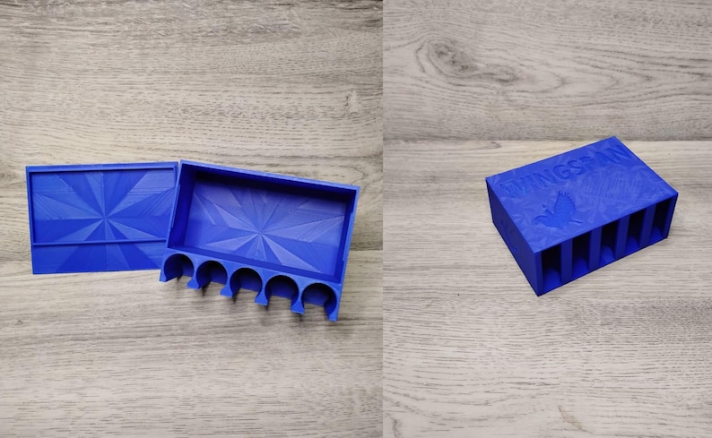 May include: A blue 3D-printed Wingspan game component organizer. The organizer has a lid and a tray with slots for game pieces. The lid and tray have a geometric design. The text "Wingspan" is visible on the top.
