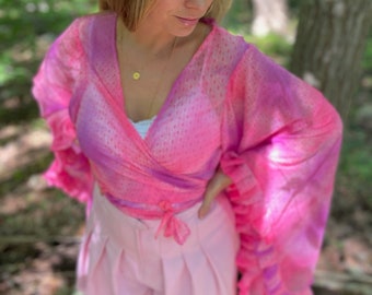 May include: A pink wrap top with long, ruffled sleeves and a matching pair of pink shorts. The top has a tie closure at the waist. The outfit is a vibrant pink colour.