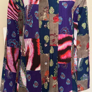 May include: A long-sleeved button-down shirt featuring a patchwork design with vertical quilted stitching. The fabric displays a mix of dark blue, brown, and vibrant pink patterns, including paisley motifs and abstract stripes throughout the garment.