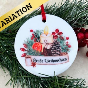 May include: White ceramic Christmas ornament with a festive design featuring a lit candle, pine branches, berries, and a scroll with the text "Frohe Weihnachten".